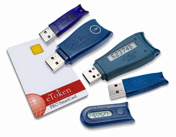 Various two-factor authentication devices including USB tokens and a smart card are scattered against a white background.