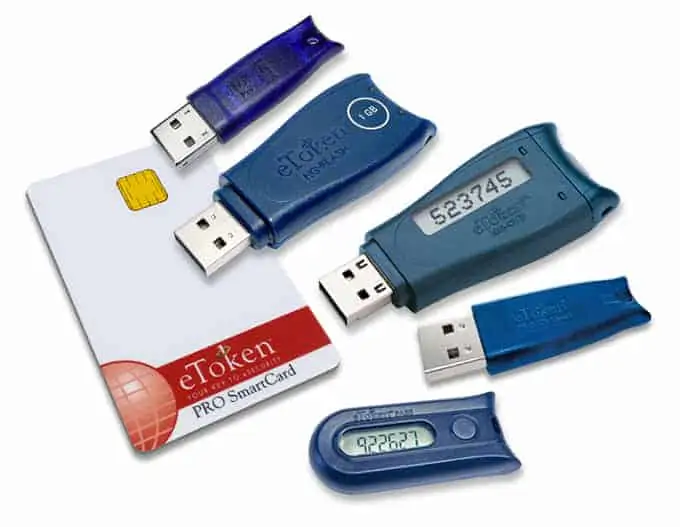 Various two-factor authentication devices including USB tokens and a smart card are scattered against a white background.