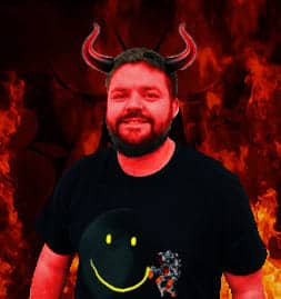 A man smiling with devil horns superimposed on his head, standing before a fiery background.